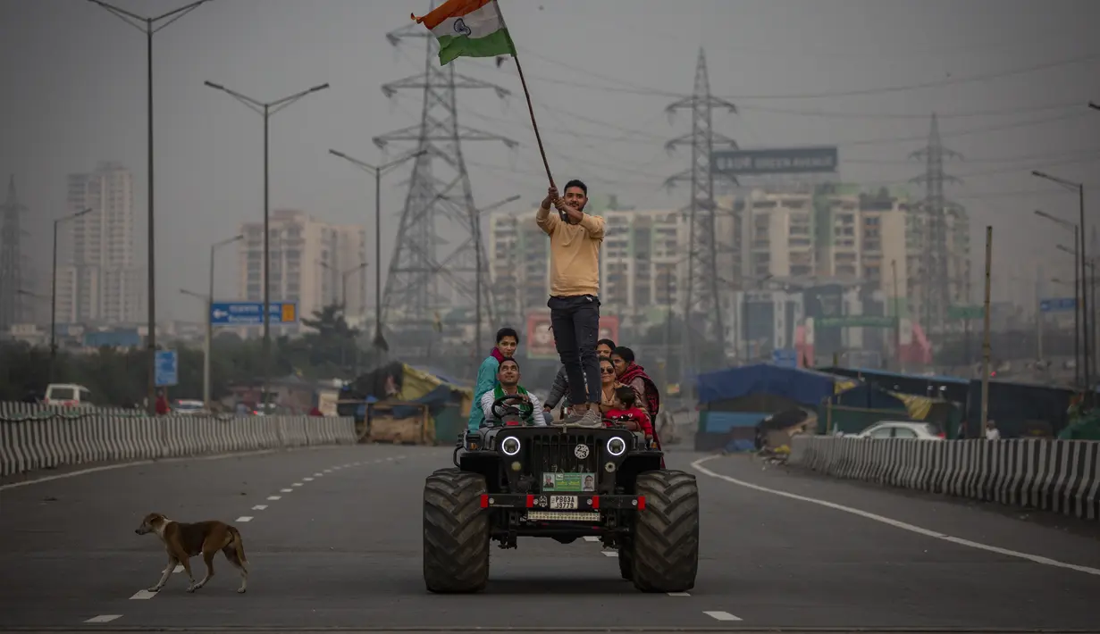 Seorang petani mengibarkan bendera India saat ia berdiri di atas kap kendaraan di jalan bebas hambatan utama di Ghazipur, pinggiran New Delhi, India, Kamis (9/12/2021). Ribuan petani India menghentikan protes mereka selama setahun pada Kamis setelah pemerintah mencabut undang-undang pertanian yang k