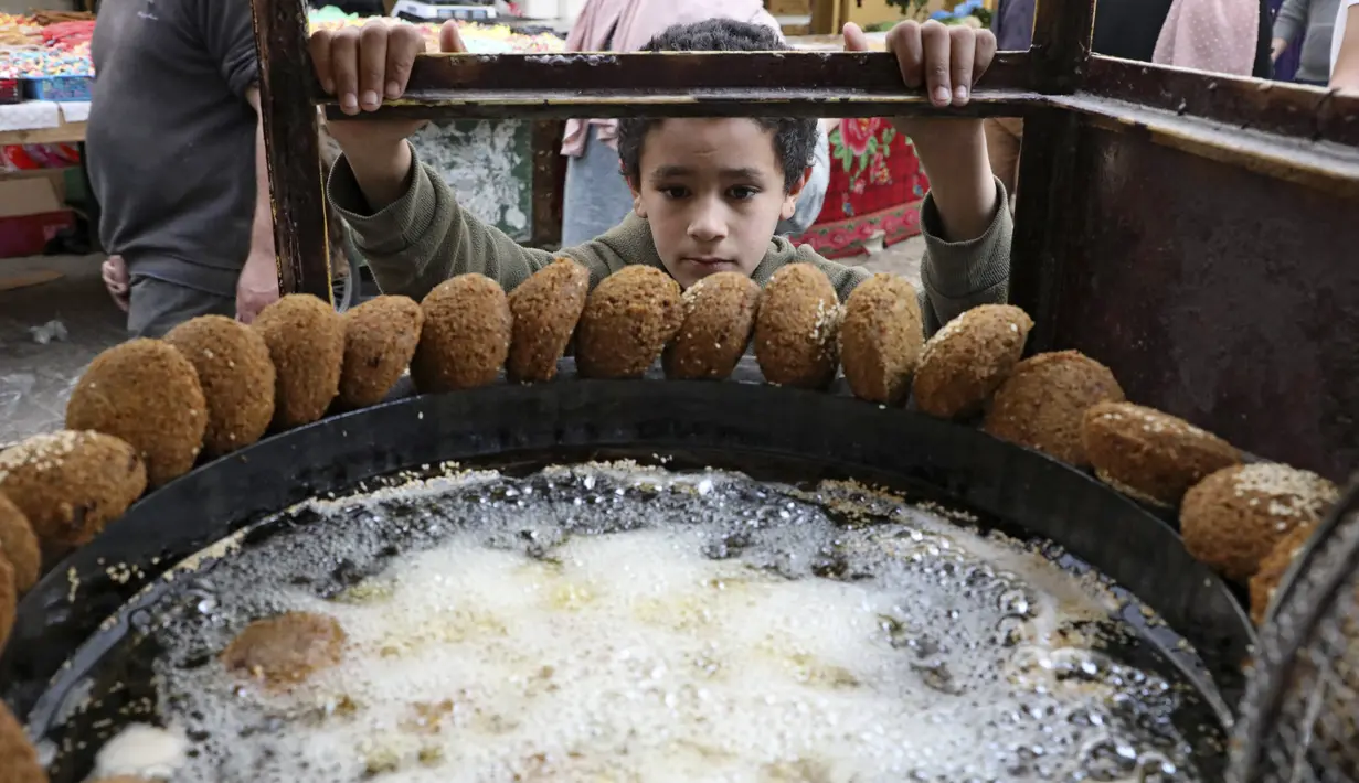 Seorang anak laki-laki Palestina menunggu sejumlah falafel di sebuah penjual di kota Hebron di Tepi Barat yang diduduki, selama bulan suci Ramadhan, Minggu (18/4/2021). Falafel adalah sebuah makanan Timur Tengah yang pada bulan Ramadhan, sering dimakan sebagai hidangan buka puasa. (HAZEM BADER/AFP)