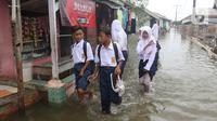 Anak-anak sekolah menerobos banjir rob yang menggenangi rumah dan tambak warga di Desa Pantai Mekar, Muaragembong, Kabupaten Bekasi, Jawa Barat, Senin (6/12/2021). Banjir rob telah menggenangi wilayah tersebut selama empat hari akibat kenaikan permukaan air laut. (Liputan6.com/Herman Zakharia)