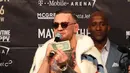 Juara mixed martial arts Conor McGregor memegang selembar uang yang dilemparkan petinju Floyd Mayweather Jr saat konferensi pers tur dunia jelang pertandingannya di Barclays Center, Brooklyn, (13/7). (Mike Lawrie/Getty Images/AFP)