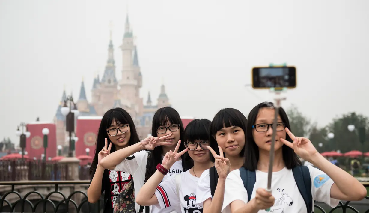 Pengunjung berpose di depan Shanghai Disney Resort di Shanghai, Tiongkok, (16/6). Taman bermain ini dibanjiri pengunjung di hari pertama pembukaan. (AFP Photo/Johannes Eisele)
