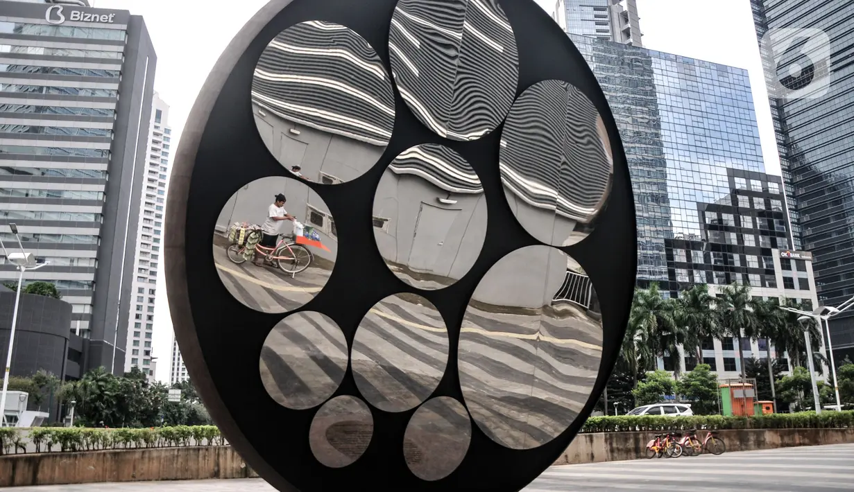 Pedagang kopi keliling terlihat dari refleksi kaca Tugu Sepeda di Jalan Jenderal Sudirman, Jakarta Pusat, Minggu (23/10/2022). Tugu Sepeda yang dibangun oleh Anies Baswedan saat menjabat Gubernur DKI Jakarta tersebut kini resmi ditampilkan ke publik. (merdeka.com/Iqbal S. Nugroho)