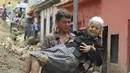 Seorang warga membawa perempuan lansia di jalan yang rusak akibat banjir dan tanah longsor yang dipicu hujan lebat di Tovar, negara bagian Merida, Venezuela, Kamis (26/8/2021). Sedikitnya 20 orang tewas akibat hujan lebat banjir yang terjadi pada Rabu, 25 Agustus. (AP Photo/Luis Bustos)