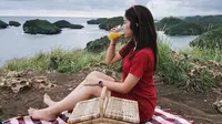 Fay Nabila tampak cantik dengan busana berwarna merah. Berpose di Pantai Kasap yang merupakan Raja Ampatnya Pacitan layaknya sedang piknik, ia tampak sedang minum jeruk dan menikmati indahnya suasana pantai tersebut. (Liputan6.com/IG/faynabilalxndr)