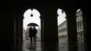 Suami istri mengenakan payung saat hujan di St. Mark's Square di Venesia, Minggu (1/3/2020). Pemerintah Italia akan melarang orang berciuman di tempat umum, berjabatan tangan dan menjaga jarak yang aman dari masing-masing lain untuk membatasi penyebaran virus corona. (AP Photo/Francisco Seco)