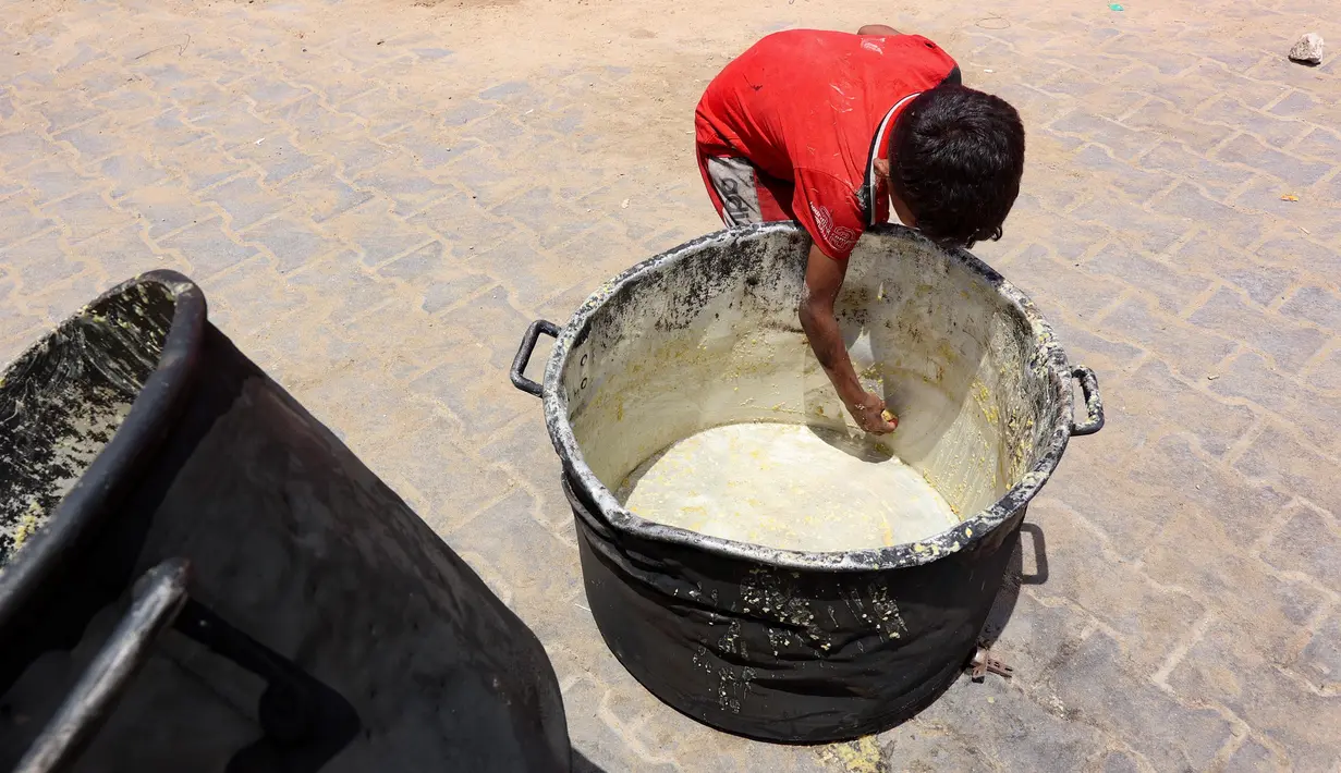 Seorang anak laki-laki Palestina mengorek sisa-sisa sup kacang miju-miju yang tersisa di dalam panci, di depan titik distribusi makanan di kamp pengungsian dekat pelabuhan Kota Gaza pada 22 Mei 2025. (Omar AL-QATTAA/AFP)