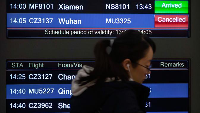Seorang pelancong melewati papan informasi penerbangan dari Wuhan yang dibatalkan di Bandara Internasional Ibu kota Beijing, 23 Januari 2020. Pemerintah China memutuskan menutup seluruh akses masuk dan keluar Kota Wuhan untuk mencegah penyebaran wabah virus corona. (AP/ Mark Schiefelbein)