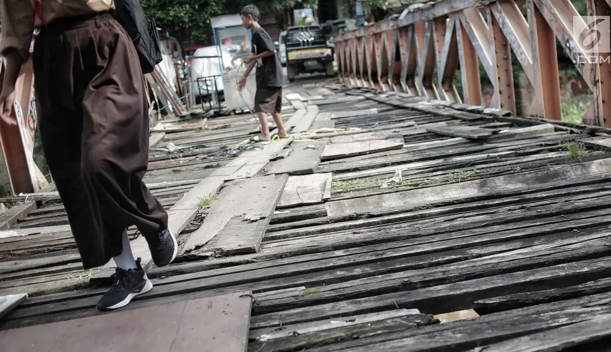 Anak anak melintasi jembatan dari kayu yang menjadi penghubung antara Jalan Karet Pasar Baru VII, Karet Tengsin dan Jalan Pam Baru, Bendungan Hilir, Tanah Abang, Rabu (30/1). (Liputan6.com/Faizal Fanani)