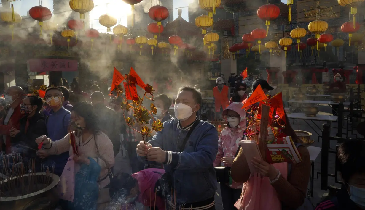 Warga yang mengenakan masker membakar dupa saat mereka berdoa di Kuil Wong Tai Sin, Hong Kong, Jumat (12/2/2021). Meskipun perayaan Imlek biasanya dilakukan dengan cara bervariasi di seluruh dunia, maka tahun ini sangat berbeda karena pandemi COVID-19. (AP Photo/Kin Cheung)