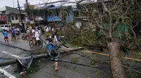 Seorang warga membawa sepeda melewati tiang listrik dan pohon yang tumbang akibat Topan Rai di kota Cebu, Filipina tengah, Jumat (17/12/2021). Lebih dari 300.000 penduduk desa telah melarikan diri ke tempat yang aman sebelum terjangan Topan Rai. (AP Photo/Jay Labra)