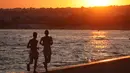 Dua orang berlari saat menikmati matahari terbenam di pantai Sampieri, Sisilia, (31/7). (AFP Photo/Ludovic Marin)