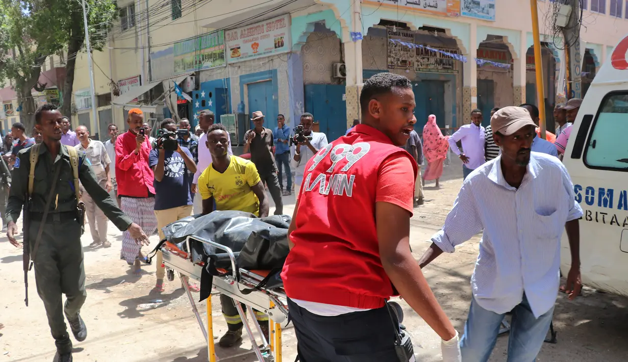 Petugas dibantu warga membawa jenazah korban di lokasi serangan bom mobil di Distrik Hamarwayne, Mogadishu, Somalia (4/2). Menurut Polisi setempat, serangan bom mobil tersebut meledak di dekat sebuah mal di pasar. (AFP Photo/Abdirazak Hussein Farah)