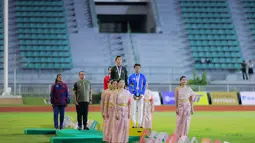 Raihan ini setelah Emilia Nova berhasil mengumpulkan total 5.497 poin sekaligus mengakhiri penantian panjangnya di nomor tersebut. Tampak dalam foto, atlet atletik Indonesia, Emilia Nova (tengah) saat prosesi penghormatan bendera usai memenangi lomba dan meraih emas nomor heptathlon (tujuh lomba) SEA Games 2025 di Stadion Supachalasai Bangkok, Thailand Selasa (16/12/2025) malam. (Bola.com/Bagaskara Lazuardi)