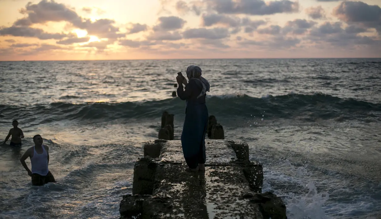 Seorang wanita mengambil gambar seorang pria yang tengah menikmati pantai Tel Aviv, Israel, Minggu (19/7/2015). Selama Idul Fitri, pemerintah Israel mengizinkan warga Palestina untuk berwisata di sepanjang garis pantai Mediterania. (REUTERS/Baz Ratner) 