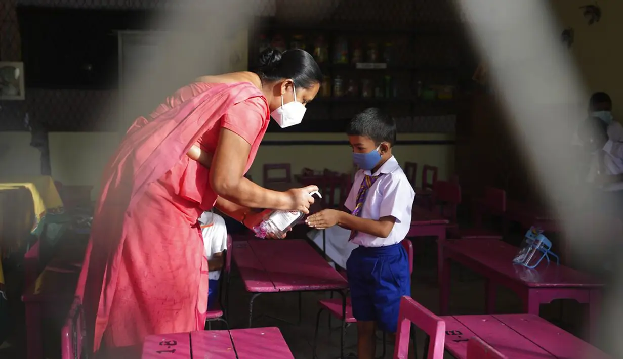 Seorang guru menyemprotkan disinfektan ke telapak tangan siswa sekolah dasar pada awal pelajaran di sebuah sekolah di Kolombo, Sri Lanka, 25 Oktober 2021. Sri Lanka memulai kembali semua sekolah dasar yang telah ditutup lebih dari enam bulan karena pandemi COVID-19. (AP Photo/Eranga Jayawardena)