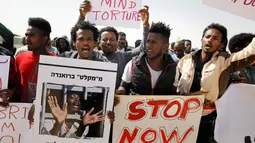 Migran Afrika membawa poster dan foto rekan mereka yang ditahan pemerintah Israel saat melakukan aksi di Penjara Saharonim, Israel (22/2). Sebelumnya, Israel mengusir puluhan ribu imigran Afrika. (AFP Photo/Menahem Kahana)