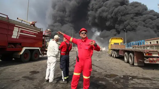 Pemadam kebakaran bekerja saat asap hitam mengepul di langit setelah ledakan dahsyat mengguncang pelabuhan dekat kota selatan Bandar Abbas, Iran, Sabtu (26/4/2025) (Mohammad Rasoul Moradi/IRNA via AP Photo)