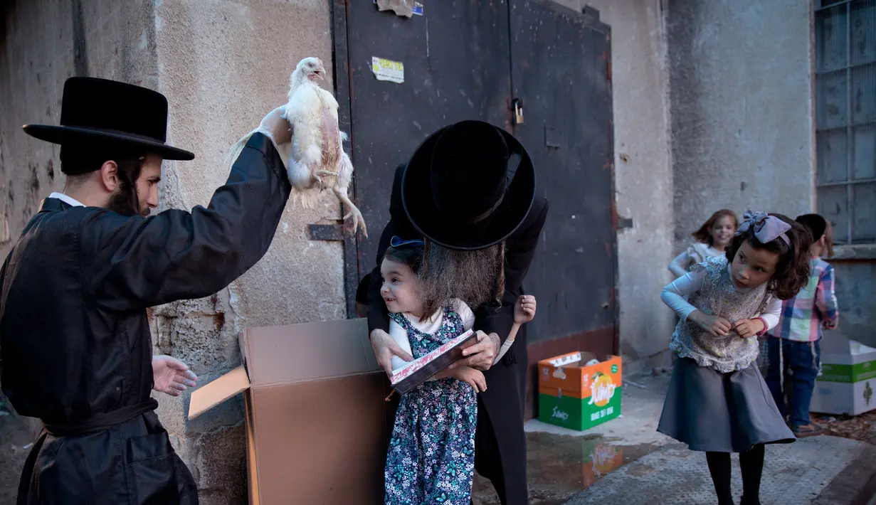 Pria Yahudi ultra-Ortodoks mengayunkan ayam memutari kepala putrinya dalam ritual Kaparot di Bnei Brak, Israel, Minggu (16/9). Ayam ini kemudian akan disembelih menjadi pengganti seseorang tersebut sebagai penebusan untuk dosa-dosanya. (AP/Oded Balilty)