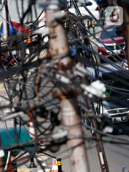 Kendaraan melintas di bawah kabel listrik dan kabel optik yang terlihat semrawut di kawasan Taman Puring, Jakarta, Jumat (3/7/2020). Tidak ada aturan yang baku membuat satu tiang listrik bisa digunakan berbagai kabel baik itu listrik ataupun optik dari berbagai provider. (Liputan6.com/Johan Tallo)