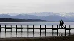 Pasangan berjalan di dermaga di depan pegunungan Alp di danau Starnberger See dekat desa Starnberg, Jerman selatan, selama cuaca musim semi dengan suhu 15 derajat pada 3 April 2018. (AFP Photo/Christof Stache)
