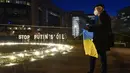 Seorang pria memegang bendera Ukraina saat berdiri dekat tanda perdamaian raksasa jelang KTT Uni Eropa dan NATO di Brussels, Belgia, 22 Maret 2022. Pengunjuk rasa meminta para pemimpin Uni Eropa memberlakukan larangan penuh terhadap bahan bakar Rusia. (AP Photo/Geert Vanden Wijngaert)