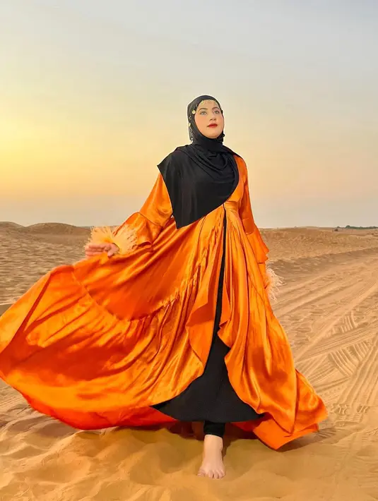 Kali ini, Tasyi tampil benar-benar seperti Arabian princess. Berlatar padang pasir, dress megah berwarna oranye yang Tasyi kenakan disempurnakan dengan hijab hitam dan aksesori emasnya. Foto: Instagram.