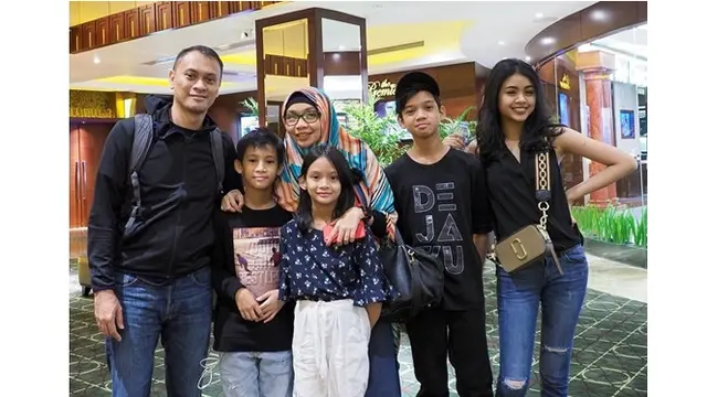 Andra dan keluarga kompak mengenakan baju berwarna gelap.