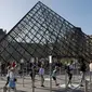 Pengunjung mengentre di piramida Louvre yang dirancang arsitek China Ieoh Ming Pei, pintu masuk ke Museum Louvre pada hari pertama pembukaan di Paris (6/7/2020). Setelah berbulan-bulan ditutup akibat lockdown Covid-19, Museum Louvre kembali dibuka pada 6 Juli 2020. (AFP/Francois Guillot)