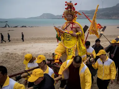 Penduduk desa menggunakan tandu membawa seorang pria berpakaian seperti Dewa Laut menuju pantai desa Fuye, Provinsi Fujian, Tiongkok (5/3). Mereka adalah komunitas nelayan setempat yang menggelar ritual kepercayaan. (AFP Photo/Johannes Eisele)