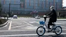 Seorang wanita bermasker mengendarai sepeda di depan kantor pusat Alibaba di Kota Hangzhou, Provinsi Zhejiang, China, Rabu (5/2/2020). Pemerintah Hangzhou memberlakukan pembatasan pergerakan bagi warganya menyusul mewabahnya virus corona. (NOEL CELIS/AFP)