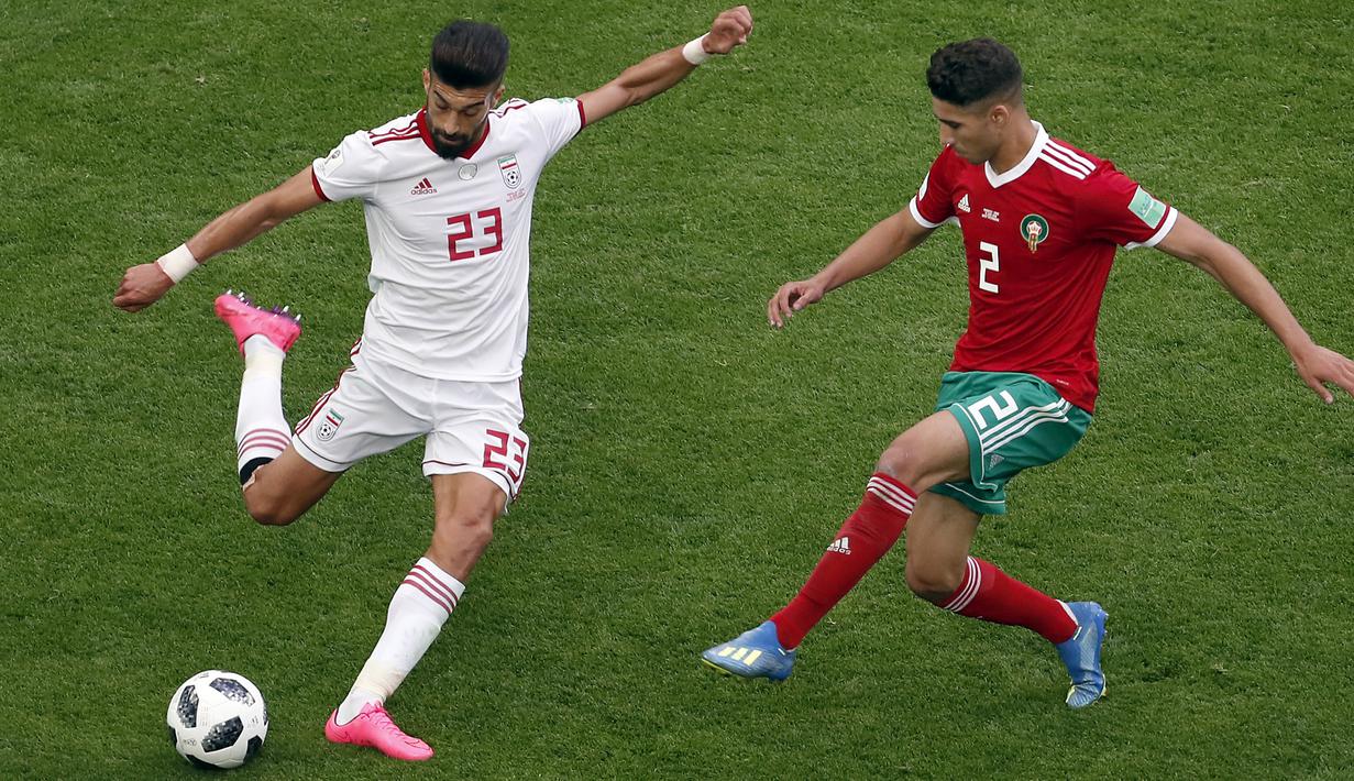 Aksi pemain Iran, Ramin Rezaeian (kiri) melepaskan tembakan saat diadang pemain Maroko, Achraf Hakimi (kanan) pada laga grup B Piala Dunia 2018 di St. Petersburg Stadium, Rusia, (15/6/2018). Iran menang 1-0. (AP/Darko Vojinovic)