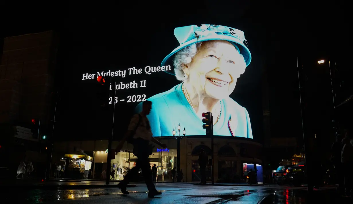 <p>Seorang pria berjalan dengan payung melewati gambar Ratu Elizabeth II yang diproyeksikan ke layar besar di Piccadilly Circus, di London, Kamis, 8 September 2022. Ratu Elizabeth II meninggal pada hari Kamis setelah 70 tahun bertahta. Dia berusia 96 tahun. (AP Photo/Alberto Pezzali)</p>