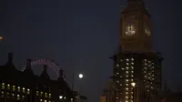 Bulan purnama pertama tahun ini atau Wolf Moon terlihat di belakang London Eye dan tampilan jam saat perbaikan Menara Elizabeth, yang dikenal sebagai Big Ben dan Gedung Parlemen, di London, Senin (17/1/2022). Wolf Moon adalah sebutan untuk bulan purnama pertama di Januari. (AP Photo/Matt Dunham)