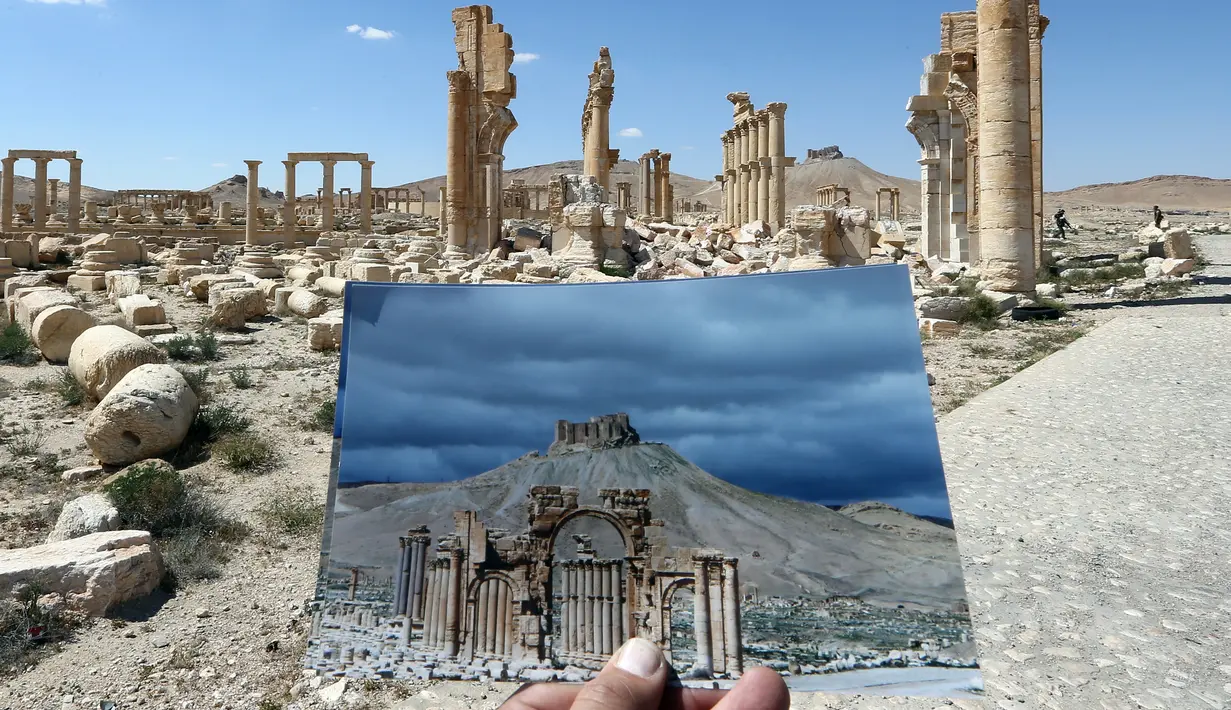 Seorang fotografer memegang foto Arc du Triomphe yang diambil pada tanggal 14 Maret 2014 di depan sisa-sisa kuil bersejarah setelah dihancurkan oleh ISIS pada Oktober 2015 di kota kuno Palmyra, Suriah, 31 Maret 2016. (Joseph EID/AFP)