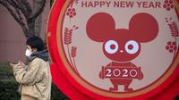 Seorang perempuan mengenakan masker berdiri dekat layar untuk perayaan Imlek Tahun Tikus Logam di Beijing, 22 Januari 2020. Otoritas kesehatan China mendesak orang-orang menghindari keramaian dan pertemuan publik di Wuhan, kota yang menjadi pusat penyebaran wabah virus corona. (AP/Mark Schiefelbein)