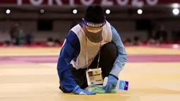Seorang petugas membersihkan dan mendisinfektan matras pada pertandingan babak penyisihan -81kg judo putra antara Saeid Mollaei dari Mongolia dan Murad Fatiyev dari Azerbaijan selama Olimpiade Tokyo 2020 di Nippon Budokan di Tokyo pada 27 Juli 2021. (Jack GUEZ / AFP)