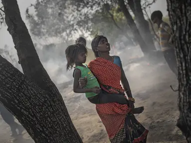 Seorang wanita menggendong putrinya saat terjadi kebakaran di daerah kumuh di Noida, pinggiran New Delhi, India, Minggu (11/4/2021). Dua anak tewas dan lebih dari 150 gubuk kumuh yang sebagian besar dihuni oleh para pemulung dalam kebakaran pada Minggu sore. (AP Photo/Altaf Qadri)