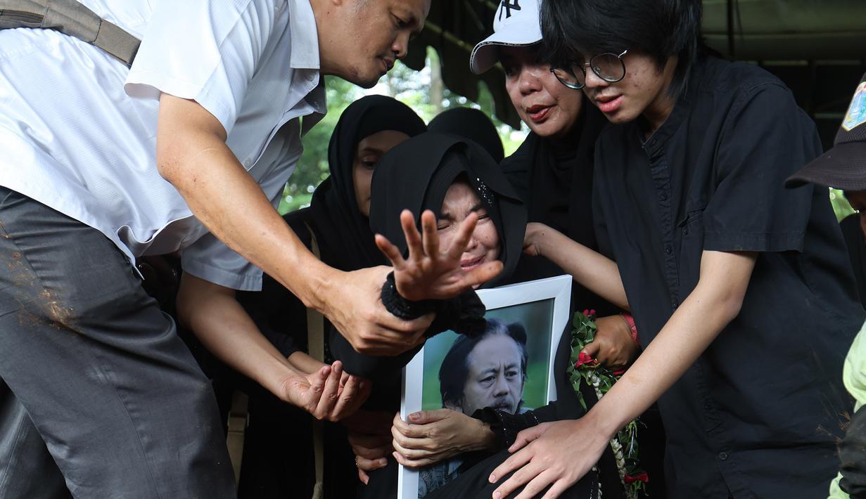 Karina Ranau (tengah) menangis saat menyaksikan pemakaman suaminya, Epy Kusnandar, di Tempat Pemakaman Umum (TPU) Jeruk Purut, Jakarta Selatan, Kamis (4/12/2025) pagi. Setelah disemayamkan di rumah duka, jenazah Epy Kusnandar dimakamkan di Tempat Pemakaman Umum (TPU) Jeruk Purut, Jakarta Selatan. (Kapanlagi.com/Budy Santoso)