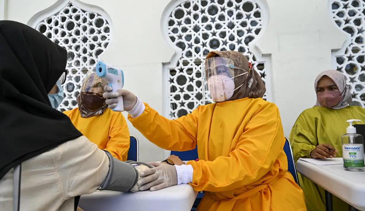 Seorang petugas kesehatan mengukur suhu tubuh seorang wanita sebelum memberinya vaksin virus corona COVID-19 Sinovac saat pelaksanaan vaksinasi di Masjid Raya Baiturrahman, Banda Aceh, Aceh, Selasa (7/9/2021). (CHAIDEER MAHYUDDIN/AFP)