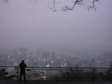 Seorang pria melihat ke arah gedung-gedung yang diselimuti kabut saat ia mengunjungi Menara Namsan pada hari yang tercemar di Seoul, Korea Selatan, Rabu (15/12/2021). (AFP/Anthony Wallace)