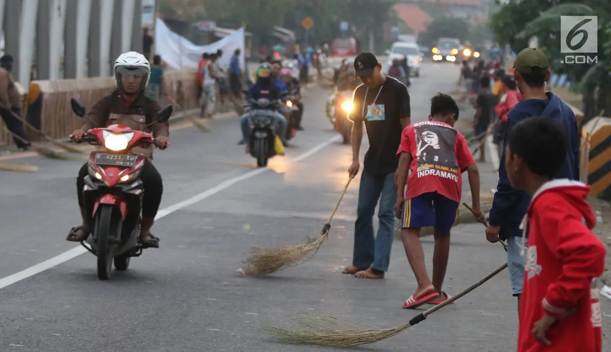 Warga membawa sapu menunggu pengguna jalan memberi sedekah dengan melempar uang di Jembatan Sewo, Jalur Pantura Sukra Indramayu, Jawa Barat, Senin (3/6/2019). Kehadiran pencari sedekah tersebut biasanya kian bertambah banyak saat menjelang arus mudik Lebaran. (Liputan6.com/Herman Zakharia)