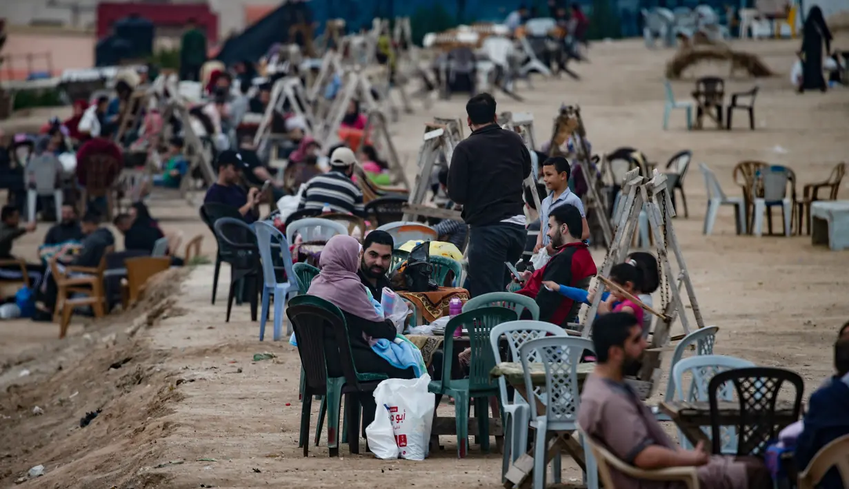 Warga Palestina berkumpul untuk berbagi makanan buka puasa selama bulan suci Ramadan, saat pandemi virus corona, di sepanjang pantai kota Gaza pada 13 Mei 2020. Mereka menunggu waktu berbuka puasa sambil menyaksikan matahari terbenam. (Photo by MAHMUD HAMS / AFP)