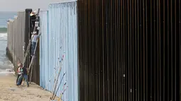 Sejumlah orang mengecat pagar perbatasan antara Meksiko dan Amerika Serikat di Playas Tijuana, Meksiko (10/12). Tembok dan pagar pembatas ini dibuat untuk mencegah masuknya imigran gelap Meksiko ke Amerika Serikat. (Reuters/Jorge Duenes)