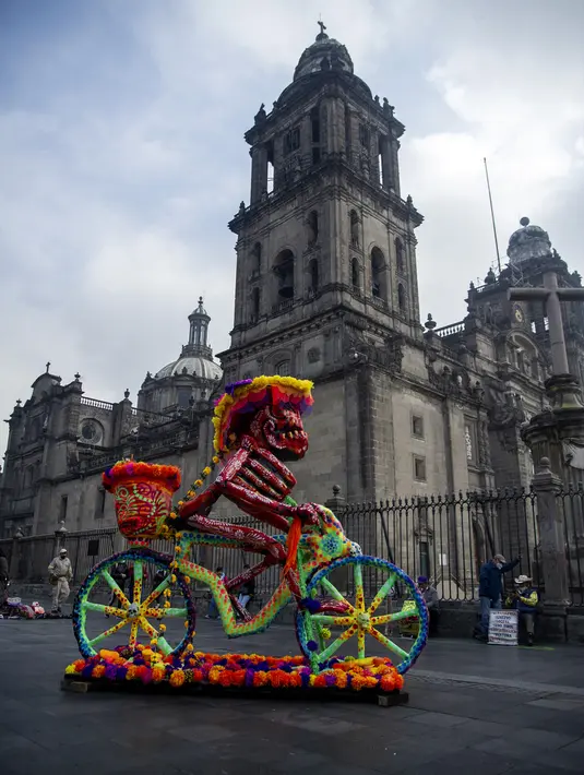 Kerangka naik sepeda dipamerkan di depan Katedral Metropolitan saat pameran Fridacraneos, tengkorak raksasa yang dilukis untuk menghormati mendiang seniman Meksiko Frida Kahlo, sebagai bagian dari perayaan Hari Kematian di Monumen Revolusi, Mexico City, Meksiko, 29 Oktober 2021. (Claudio CRUZ/AFP)