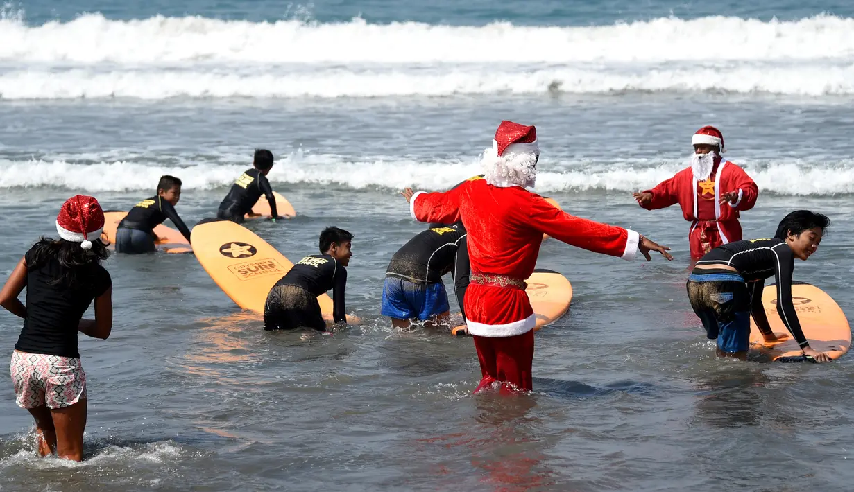 Pelatih selancar mengenakan kostum Santa Claus saat mengajar anak-anak untuk berselancar di di Pantai Kuta, Bali, Senin (10/12). Setiap tahunnya, ribuan wisatawan mendatangi Bali saat menjelang natal dan tahun baru. (AFP PHOTO / Sonny Tumbelaka)