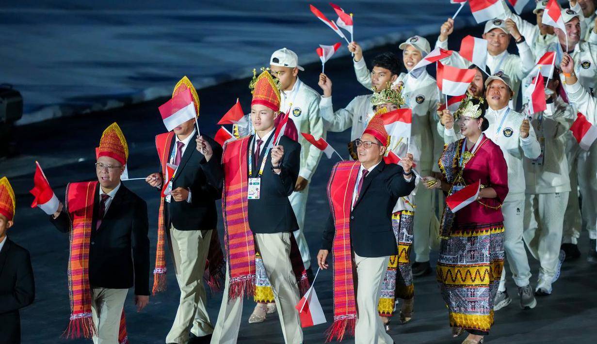 Kontingen Indonesia tampil mengunakan setelan formal hitam, Ulos, dan ikat kepala adat Sumatera Utara dan kebaya merah yang dipadukan dengan kain Tapis dan mahkota Siger Lampung di Opening Ceremony SEA Games Thailand 2025 yang digelar di Rajamanggala Stadium pada Selasa (9/12/2025) malam WIB. (Dok. NOC Indonesia)