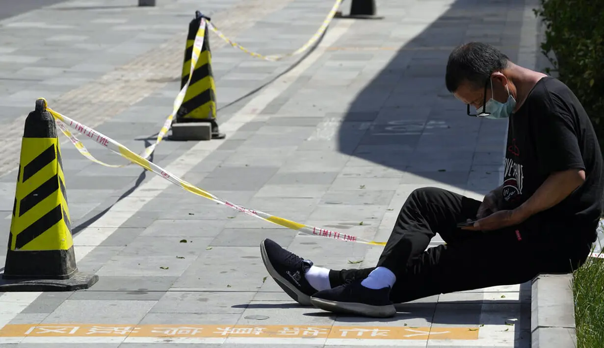 <p>Seorang warga yang mengenakan masker duduk pada trotoar di Beijing, China, Selasa (3/5/2022). China telah berpegang teguh pada pendekatan ketat 'Nol COVID' yang membatasi perjalanan, menguji massal seluruh kota, dan mendirikan fasilitas sementara yang luas untuk mencoba mengisolasi setiap orang yang terinfeksi. (AP Photo/Ng Han Guan)</p>