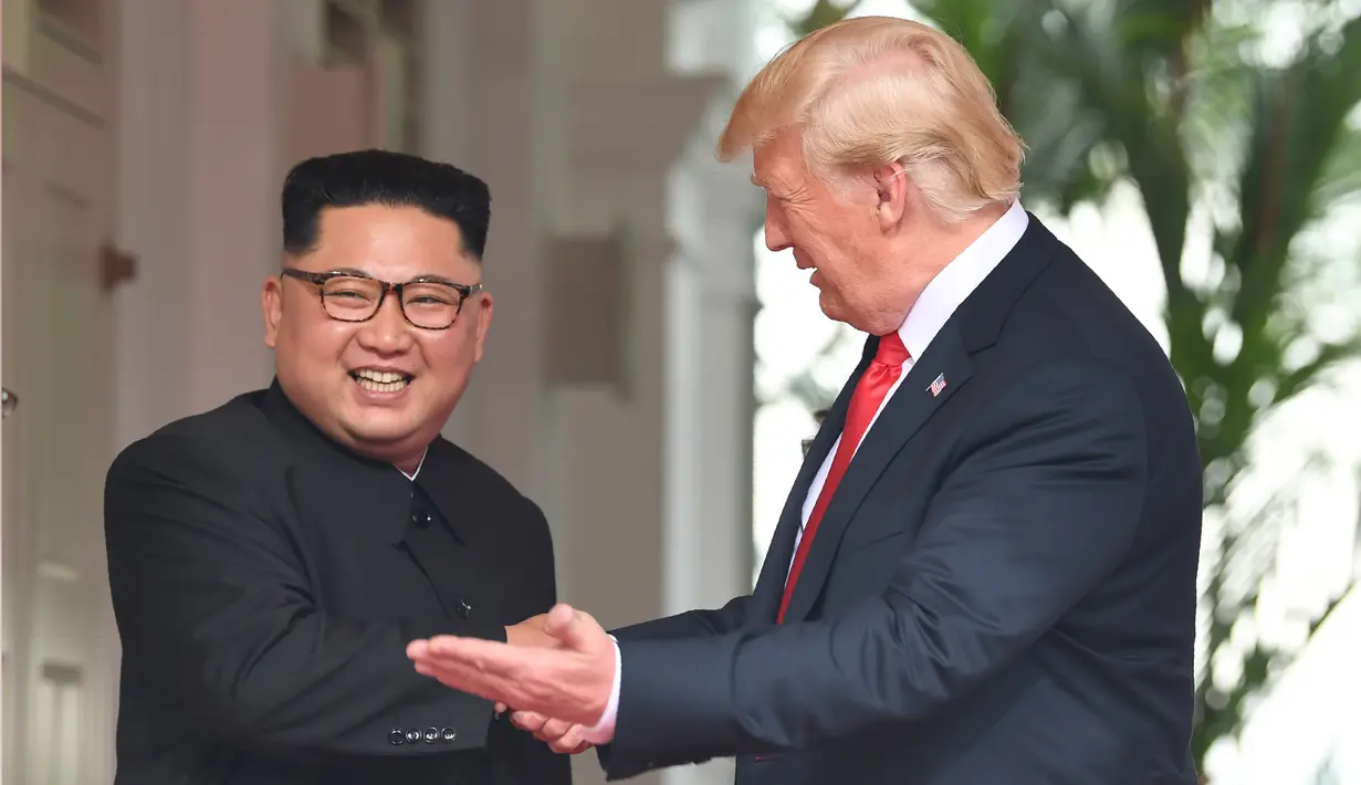 Presiden AS Donald Trump mempersilahkan Pemimpin Korea Utara, Kim Jong-un masuk ke dalam resor Capella, Pulau Sentosa, Singapura, Selasa (12/6). Pertemuan ini merupakan yang pertama kalinya bagi pemimpin AS dan Korut untuk bertatap muka. (SAUL LOEB/AFP)
