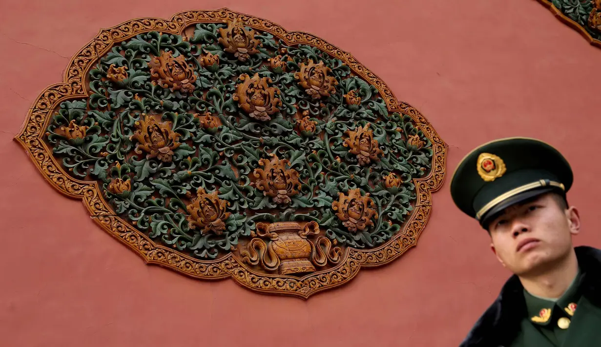 Seorang polisi paramiliter China berjaga di samping sebuah karya seni ukiran kayu yang dipajang di dinding di Kota Terlarang di Beijing, (7/3). (AP Photo/Aijaz Rahi)