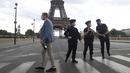 Seorang turis Rusia memegang sebotol sampanye berjalan melewati petugas polisi yang mengamankan jembatan menuju Menara Eiffel di Paris, Rabu (23/9/2020). Polisi Paris telah memblokir daerah sekitar Menara Eiffel setelah ancaman bom telepon. (AP Photo / Michel Euler)